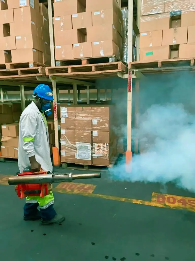 A professional fumigation expert performing pest control in a South African warehouse using advanced fogging equipment. South Africa warehouse pest control worker using a fogging machine for fumigation services.